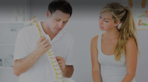 Man holding fake spine showing woman patient piece of spine as part of a Chiropractic Treatment Bethesda, MD