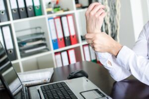 Workers' Comp Chiropractor Bethesda, MD with a man holding his wrist while sitting in front of a laptop